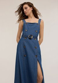 Robe en denim avec un décolleté carré, des boutons sur le devant, une fente sur le côté et une ceinture en tissu avec une boucle dorée en forme circulaire.