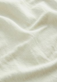 Linnedug i en lys beige farve med en let tekstureret overflade og naturlige folder, der skaber en blød, subtil dybde.