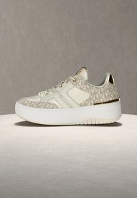 Tenis z zgornjim delom iz svetlo bež usnja z teksturiranim vzorcem logotipa MK, belo gumijasto podplatom in kovinskimi zlato barvnimi poudarki na peti.