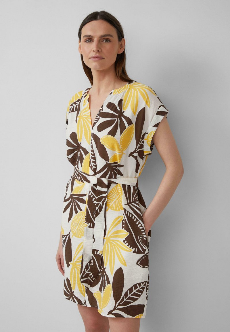 Robe à manches courtes en coton blanc avec des motifs floraux marron et jaune, présentant un décolleté en V et une taille nouée, avec des poches sur les côtés.