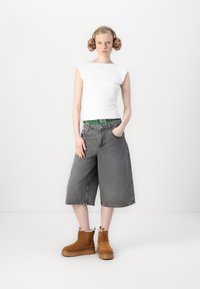 Bela prilegajoča brezrokavnik majica, sivi denim culottes in rjavi semiš gležnjarji s svetlim podplatom. Model nosi rjave puhaste ušesne zaščite.