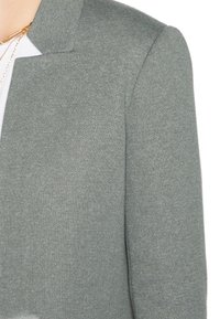 Blazer en maille gris clair avec un col structuré et un tissu texturé. Présente une coupe ajustée et des détails de couture subtils.