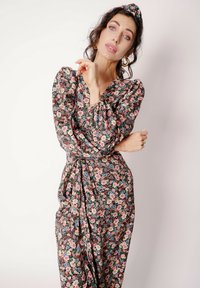 Sukienka w kwiaty na czarnym tle, z różowymi, niebieskimi i kremowymi kwiatami. Miękka tkanina, długie bufiaste rękawy oraz detal wiązania w talii.