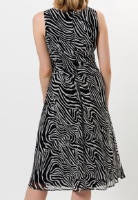 Robe sans manches à imprimé zèbre noir et blanc avec une taille cintrée, un tissu fluide et une finition au genou, présentant une texture lisse.