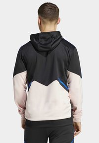 Felpa con cappuccio in alto nera e parte inferiore rosa, con accenti diagonali blu e un tessuto testurizzato.
