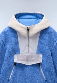 Blue fleece pullover with a cream collar and gray zippered front, featuring a prominent logo patch and side zip pockets. Textured exterior.