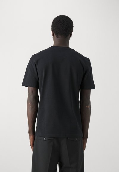 Tricou din bumbac negru, cu guler clasic și mâneci scurte, având o textură uniformă și fără modele sau logo-uri vizibile.