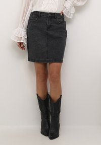 Fustă din denim neagră cu o siluetă ajustată, având buzunare frontale și închidere cu nasture. Asortată cu cizme cowboy negre.