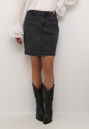 Denim skirt in black with a fitted silhouette, featuring front pockets and a button closure. Paired with black cowboy boots.