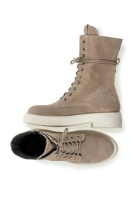 Stivali in suede taupe con lacci, alto al polpaccio, punta arrotondata e suola spessa bianca. Presenta occhielli in argento e un occhiello per il pull sul retro.