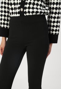 Svarta leggings i ett mjukt, elastiskt tyg, med en hög midja. Bärs tillsammans med en svart och vit mönstrad cardigan.