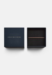 Scatola di gioielli blu navy con logo dorato. Contiene un bracciale su un cuscinetto di velluto nero, caratterizzato da un design delicato e accenti scintillanti.