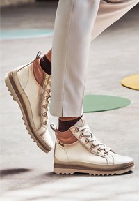 Baskets montantes en cuir blanc cassé avec des accents marron, col rembourré, bout arrondi et semelle texturée. Fermeture zippée latérale et design à lacets.