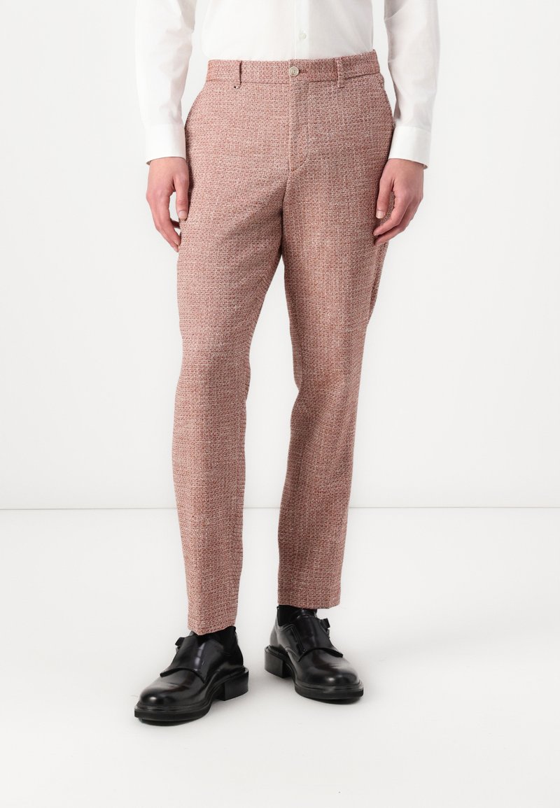 Pantalons fuselés en tissu texturé rose et blanc, dotés d'une fermeture à bouton, de passants de ceinture et de poches latérales, associés à des chaussures noires.