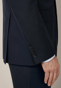 Granatowa marynarka o gładkiej fakturze, z sześcioma guzikami na mankietach i klasycznym krojem. Minimalistyczna i o prostym fasonie.