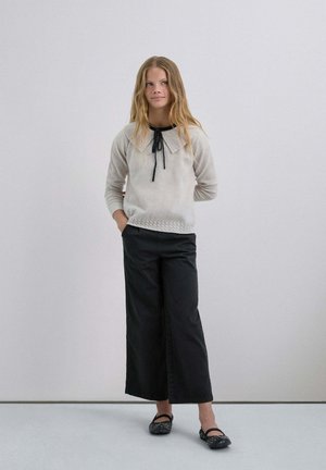 Suéter crema con un cuello alámbrico, detalle de corbata negra y dobladillo texturizado. Combinado con pantalones anchos negros y bailarinas negras con embellishments.