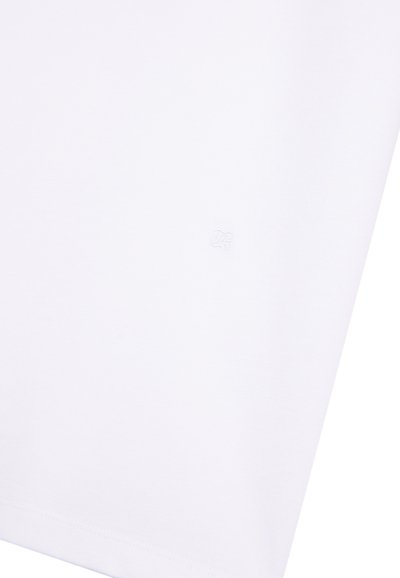 Primo piano di un tessuto bianco con un sottile logo ricamato in bianco vicino al centro e orlo cucito visibile sul bordo inferiore.