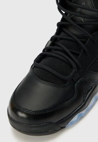 Baskets de sport noires avec un dessus en cuir lisse, des panneaux en mesh texturé et des lacets noirs. Caractérisées par une semelle en caoutchouc translucide.