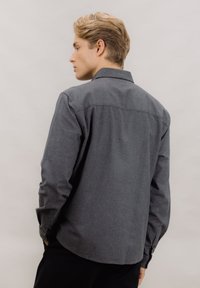 Grå langermet skjorte i et mykt stoff med knappestolpe, som har en jevn tekstur og avrundet kant bak.