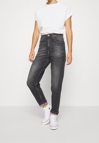 Hög midja, mörkgrå denimjeans med rak benform. Uppvikta nederkanter med röd söm. Matchas med en vit t-shirt med kort ärm och vita sneakers.