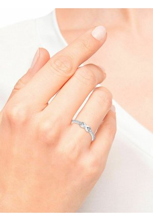 Anello in argento con design intrecciato, caratterizzato da piccole pietre preziose trasparenti, profilo testurizzato, indossato su una mano con smalto neutro.