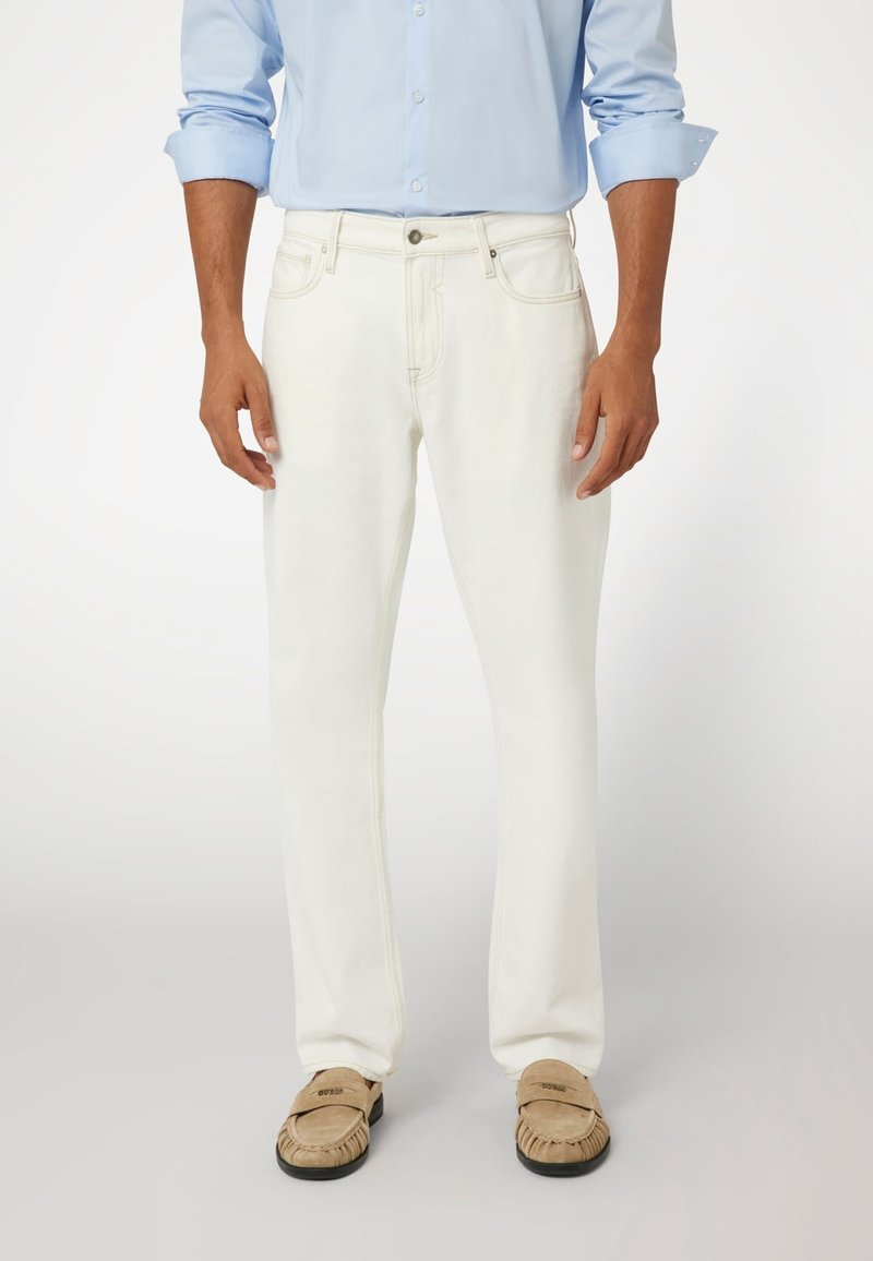 Baltos džinsinės kelnės su tiesiu kirpimu, lengvu nudilimu ir matomomis siūlėmis. Sujungtos su bežinėmis mokasinais.