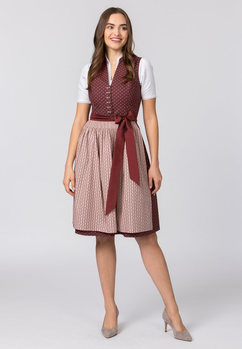 Traditionelles Kleid mit einem taillierten burgunderfarbenen Oberteil mit Knöpfen und einem gemusterten beigen Rock, der an der Taille mit einem passenden Band geschnürt ist.