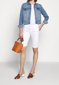 Chaqueta de mezclilla, camiseta blanca, pantalones cortos blancos, bolso de cuero marrón y mules con patrón de serpiente y tacones blancos. Atuendo casual de verano.