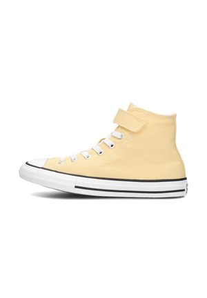 Zapatillas altas de lona suave amarilla con una correa, ojales blancos y puntera y suela de goma blanca clásica con detalles en negro.