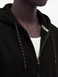 Gros plan d'une personne portant un sweat à capuche noir non zippé avec des cordons à motifs sur une chemise blanche côtelée.