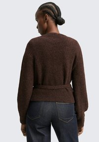 Bruin gebreid sweater met een geribbelde tailleband en strik, met een losse pasvorm en lange mouwen, gecombineerd met donkerblauwe spijkerbroek.