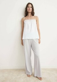 Witte camisole met kantafwerking, gecombineerd met lichtgrijze wijde broek. De stof lijkt zacht met een gladde textuur.