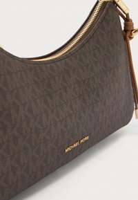 Καφέ τσάντα ώμου με ανάγλυφο μοτίβο λογότυπου, χρυσά μεταλλικά στοιχεία και κλείσιμο με φερμουάρ. Διαθέτει δερμάτινη λεπτομέρεια και ανάγλυφο λογότυπο.