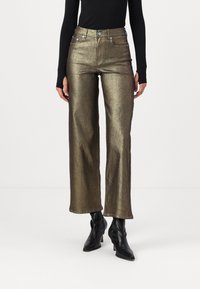 Jeans anchos de metalizado dorado con cintura alta, con bolsillos frontales, cierre con cremallera y herrajes en plata. Combinados con botas de tobillo negras y de punta.