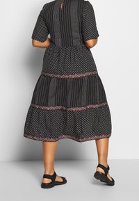 Vestido negro con mangas cortas, falda en capas, patrones intrincados y bordados coloridos en el dobladillo. Combinado con sandalias negras.