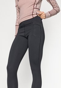Leggings de sport noirs avec une texture lisse, une poche latérale et des coutures contrastées. Portés avec un haut à motifs dans des couleurs douces.