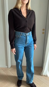 Μαύρο πουκάμισο με κουμπιά και μαλακή υφή, συνδυασμένο με ψηλόμεσα μπλε τζιν. Τα τζιν έχουν ίσια γραμμή και ανοιχτό χρώμα. Μαύρες λοφίτσες ολοκληρώνουν την εμφάνιση.