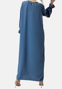 Lång, flödande blå klänning gjord av mjukt tyg. Har långa ärmar med ihopsydde manschetter och en nyckelhålsöppning bak.