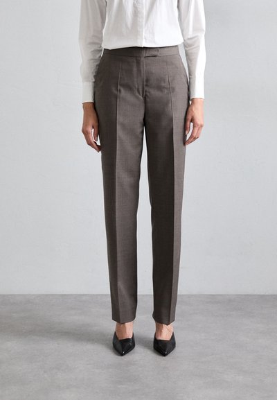 Pantaloni marroni su misura con gamba dritta, texture sottile e pieghe, abbinati a tacchi neri a punta.