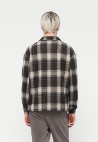 Flannel shirt in dark gray and beige plaid pattern. Features a collar, long sleeves, and relaxed fit. Soft texture and boxy shape.
