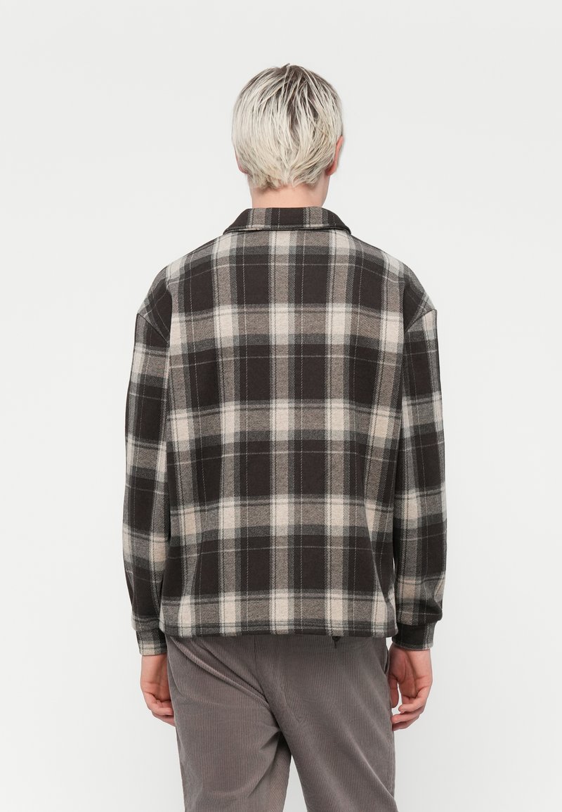 Camicia in flanella a fantasia scozzese grigio scuro e beige. Caratterizzata da colletto, maniche lunghe e vestibilità comoda. Texture morbida e forma ampia.