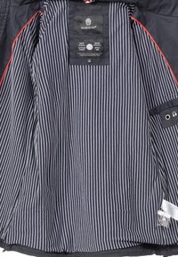 Tmavě modrá venkovní bunda s pruhovanou vnitřní podšívkou, obsahující štítek s názvem značky, rokem a pokyny pro péči. Červené akcenty u okrajů.