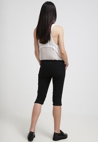 Černé oříznuté džíny s úzkým střihem, spárované s bílým tílkem s nabíraným detailem na zádech, nošeno s černými botami.