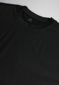 T-shirt noir à col rond et manches courtes posé à plat, montrant l'encolure et la partie supérieure de la poitrine avec une étiquette intérieure visible.