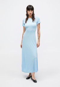 Svetlomodré šaty po kolená z hladkej látky; majú krátke rukávy, okrúhly výstrih a bočné rozparky. Celý vzhľad dopĺňajú čierne baleríny.