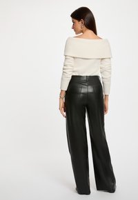 Maglione leggero color crema a spalle scoperte con una finitura testurizzata, abbinato a pantaloni in pelle neri a vita alta e gamba ampia con tasche posteriori.