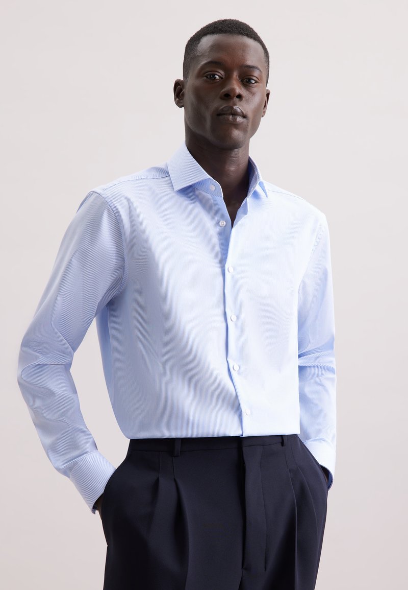 Camicia azzurra chiaro con un sottile motivo a righe, maniche lunghe e colletto classico, abbinata a pantaloni scuri su misura.