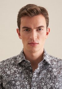 Szara koszula w kwiatowy wzór z czarno-białymi motywami roślinnymi, z kołnierzykiem typu spread i zapięciem na guziki, na neutralnym tle.