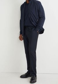 Veste zippée marine avec col montant, portée sur un t-shirt assorti à col rond et un pantalon à taille élastiquée ; associée à des mocassins noirs.