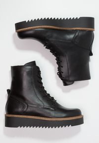 Botas de cuero negro hasta el tobillo con suela de plataforma en zigzag, diseño de cordones, punta redondeada y costuras en contraste color bronce sobre la suela.